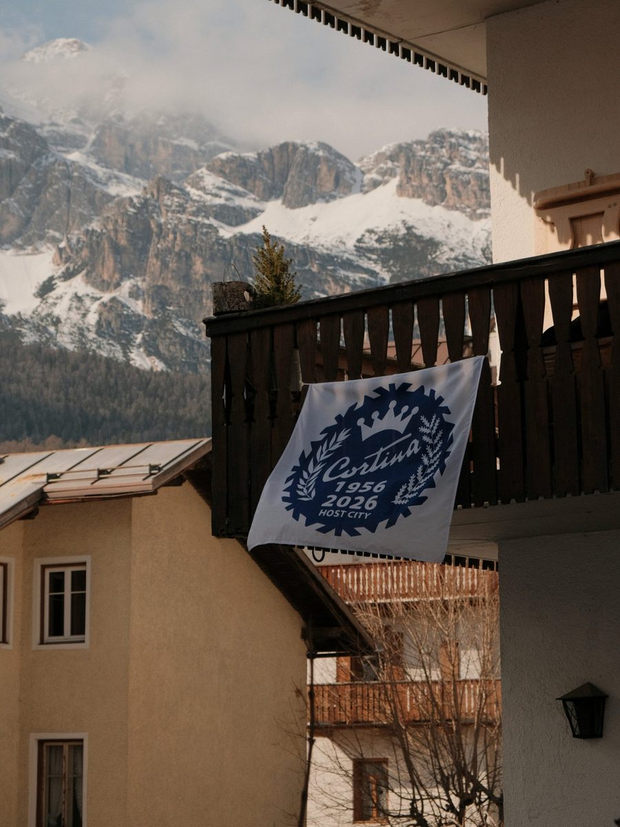 A Cortina host city flag on a wooden balcony, with the Dolomites behind